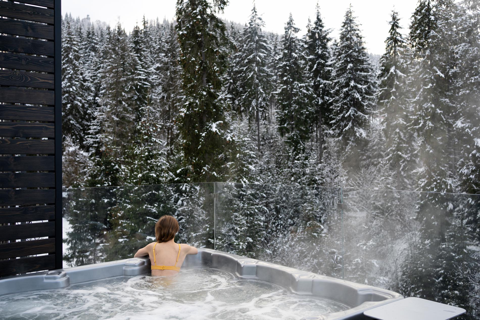 A young woman relaxes in a hot tub with a jacuzzi in the winter outdoors, sitting on back and enjoying the view of the snowy forest. Concept of winter rest in hot bath on nature